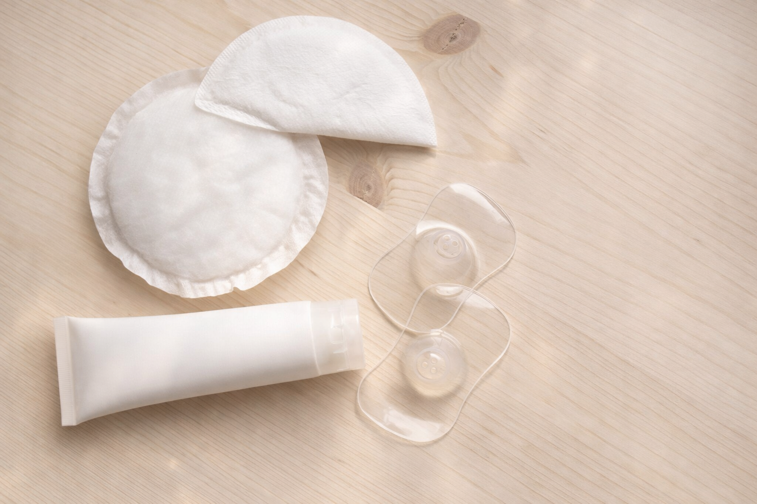 Breastfeeding care essentials including nipple cream and silicone nipple shields arranged on a soft wooden background.